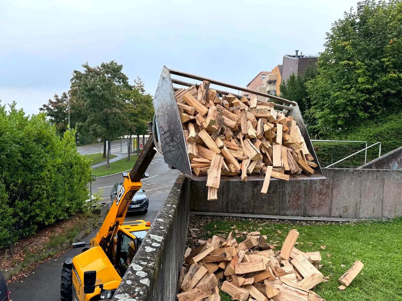 Teleskoplader kippt Brennholz über eine Gartenmauer